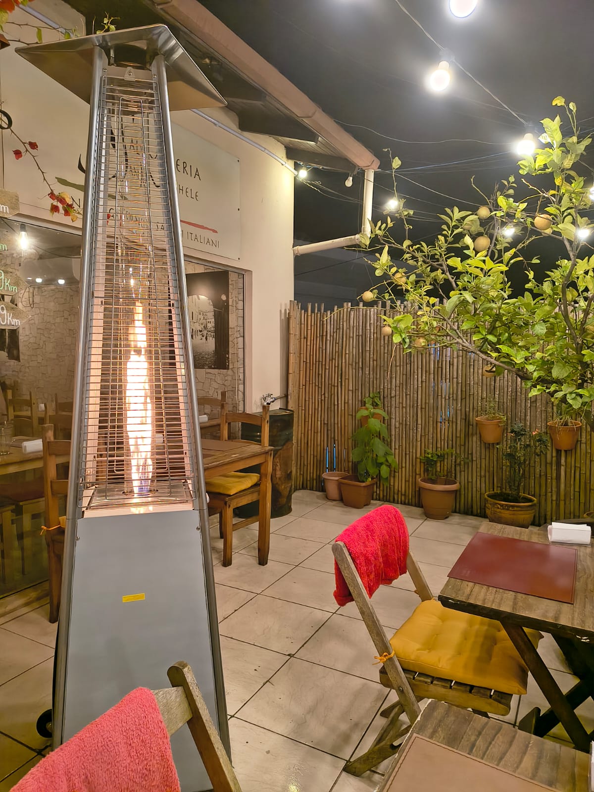 Ambiente acolhedor da Salumeria San Michele com mesas vazias, plantas e iluminação noturna